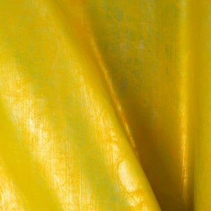May include: A close-up of a yellow fabric with a textured, crinkled surface. The fabric has a subtle sheen and appears to be made of a lightweight material.
