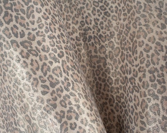 May include: A close-up of a fabric with a leopard print pattern. The fabric is a light brown colour with dark brown spots. The fabric has a shimmery, glittery texture.