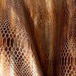 May include: Close-up of a brown and gold fabric with a snakeskin pattern.