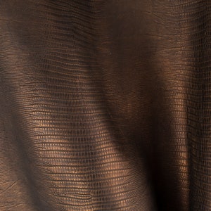 May include: Close-up of a brown textured fabric with a subtle sheen. The fabric has a repeating pattern of small squares.