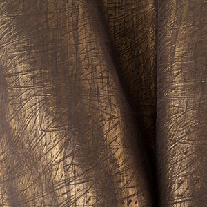May include: Close-up of a brown fabric with a gold metallic sheen. The fabric has a textured, embossed pattern that resembles brushstrokes.