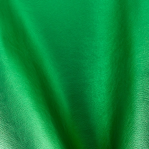 Op de afbeelding: Close-up van een getextureerde, groene lederen stof. De stof heeft een glad, glanzend oppervlak en een subtiele, gerimpelde textuur.