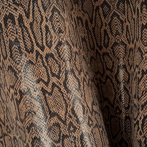 Op de afbeelding: Close-up van een bruine en zwarte slangenhuidstof met een textuurpatroon.