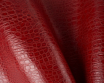 May include: Close-up of a red crocodile embossed leather texture. The leather is folded in half, showing the texture from both sides.