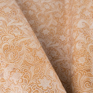 May include: A close-up of a tan fabric with a white floral pattern. The fabric is folded in half, showing the pattern on both sides.