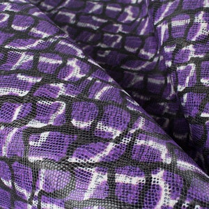 Könnte beinhalten: Nahaufnahme eines strukturierten Stoffes mit einem reptilienartigen Muster. Das Design zeigt ein sich wiederholendes Muster aus lila, schwarzen und weißen Formen, das einen visuell auffälligen Effekt erzeugt. Der Stoff ist gefaltet und zeigt seine Textur und Tiefe.