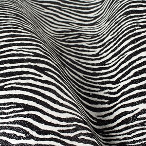 Puede incluir: Tela de estampado de cebra en blanco y negro con textura brillante. La tela está doblada y tiene un patrón ondulado.