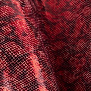 May include: Red snakeskin fabric with a textured, grid-like pattern. The fabric is folded and draped, creating a wavy, flowing effect.