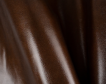 May include: Close-up of brown leather with a textured surface. The leather is folded and has a slight sheen.