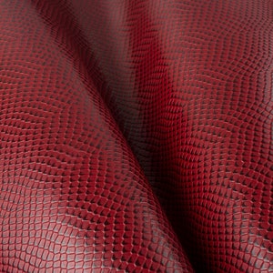 Puede incluir: Tela de imitación de piel de serpiente roja con un patrón texturizado. La tela está doblada en forma de onda.