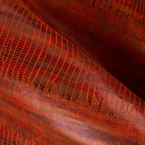 Puede incluir: Primer plano de una tela texturizada de color rojo anaranjado con un patrón de piel de cocodrilo. La tela está doblada y tiene un ligero brillo.