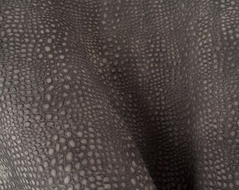 Op de afbeelding: Close-up van een donkergrijze, textuurrijke stof met een patroon van kleine, verhoogde cirkels.
