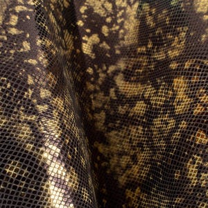 Puede incluir: Primer plano de una tela con un patrón de piel de serpiente. La tela es de color marrón oscuro con un brillo metálico dorado. El patrón está formado por pequeñas escamas superpuestas.