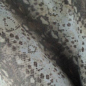 May include: A close-up of a white fabric with a delicate lace pattern. The fabric has a subtle brown snakeskin print underneath the lace.