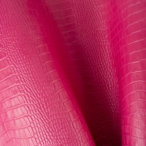Puede incluir: Primer plano de una tela texturizada rosa con un patrón de piel de cocodrilo.