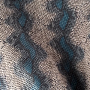 Op de afbeelding: Close-up van een textuurdoek met een slangenhuidpatroon in grijstinten en blauw.
