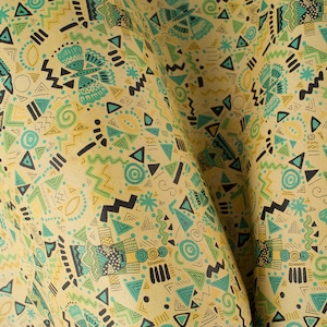 May include: A yellow fabric with a repeating pattern of geometric shapes in shades of green, blue, and black. The fabric is folded in half, creating a textured effect.