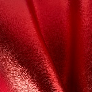 May include: Close-up of a red leather fabric with a textured surface. The fabric is folded and has a soft, smooth feel.