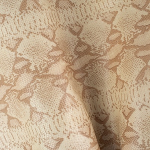 Puede incluir: Primer plano de un patrón de piel de serpiente beige y marrón. El material de cuero sintético tiene una superficie texturizada con un diseño de escamas repetido. La paleta de colores incluye beige claro y varios tonos de marrón.