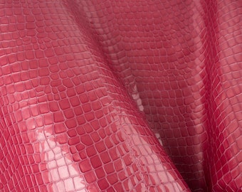 May include: Close-up of a pink crocodile embossed leather fabric. The leather has a glossy finish and a textured pattern.