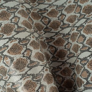 May include: A close-up of a white fabric with a brown and black snake skin pattern.