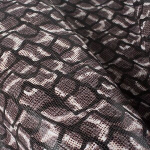 Può includere: Primo piano di un tessuto in pelle di serpente nero e bianco con un motivo testurizzato.