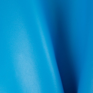 Pode incluir: Close-up de uma superfície de couro lisa e azul brilhante. O couro está dobrado no centro, criando uma curva suave e delicada.