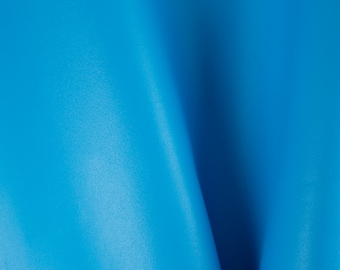 May include: A close-up of a smooth, bright blue leather surface. The leather is folded in the center, creating a soft, gentle curve.