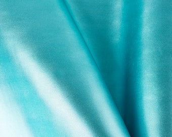 May include: A close-up of a smooth, turquoise fabric with a subtle sheen. The fabric is folded in a way that creates a soft, flowing drape.