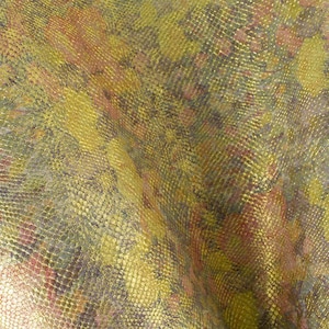 Puede incluir: Una tela texturizada con un patrón de piel de serpiente en tonos dorados, verdes y rojos.