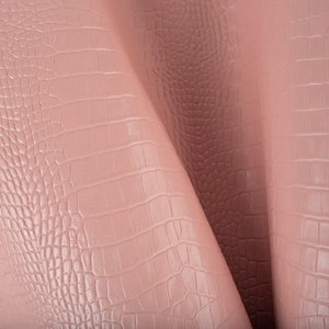 May include: Close-up of a pink faux leather fabric with a crocodile embossed pattern.