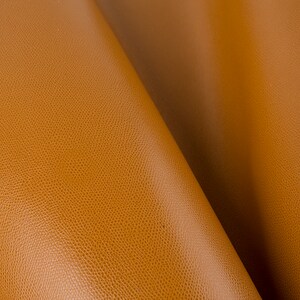 May include: Close-up of a textured, brown leather material. The leather has a subtle grain pattern and a warm, rich tone.