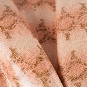 Puede incluir: Primer plano de una tela de color melocotón con un patrón de piel de serpiente marrón. La tela está doblada y tiene una superficie texturizada.