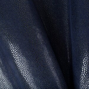 Op de afbeelding: Close-up van een donkerblauwe stof met een getextureerd, geëmbost patroon dat lijkt op schubben. De stof heeft een subtiele glans en voelt glad en zacht aan.