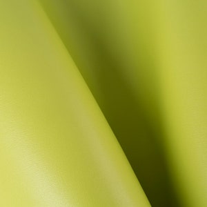 Può includere: Primo piano di un tessuto verde lime liscio e testurizzato. Il tessuto è piegato a metà, creando una forma morbida e curva.