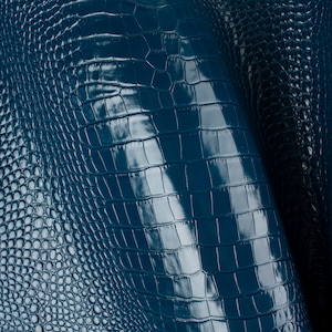 May include: Close-up of teal blue crocodile embossed leather. The leather has a glossy finish and a textured pattern.