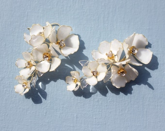 May include: A pair of white flower earrings with gold wire and crystal accents. The earrings are made of delicate, layered flowers.