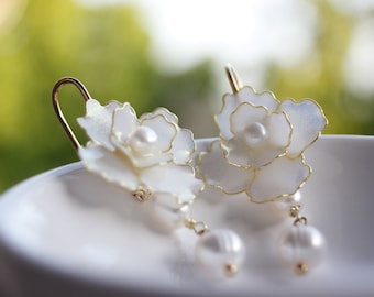 May include: A pair of white flower-shaped earrings with gold accents and pearl drops.