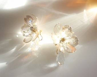 May include: A pair of delicate flower-shaped earrings with clear glass petals and gold accents. Each earring features a small crystal drop.
