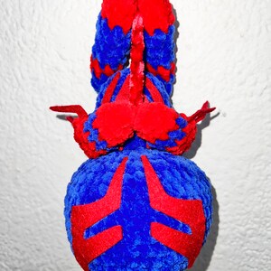 May include: A blue and red crocheted plush toy shaped like a spider hanging from a white ceiling. The spider has a red and blue pattern on its body.
