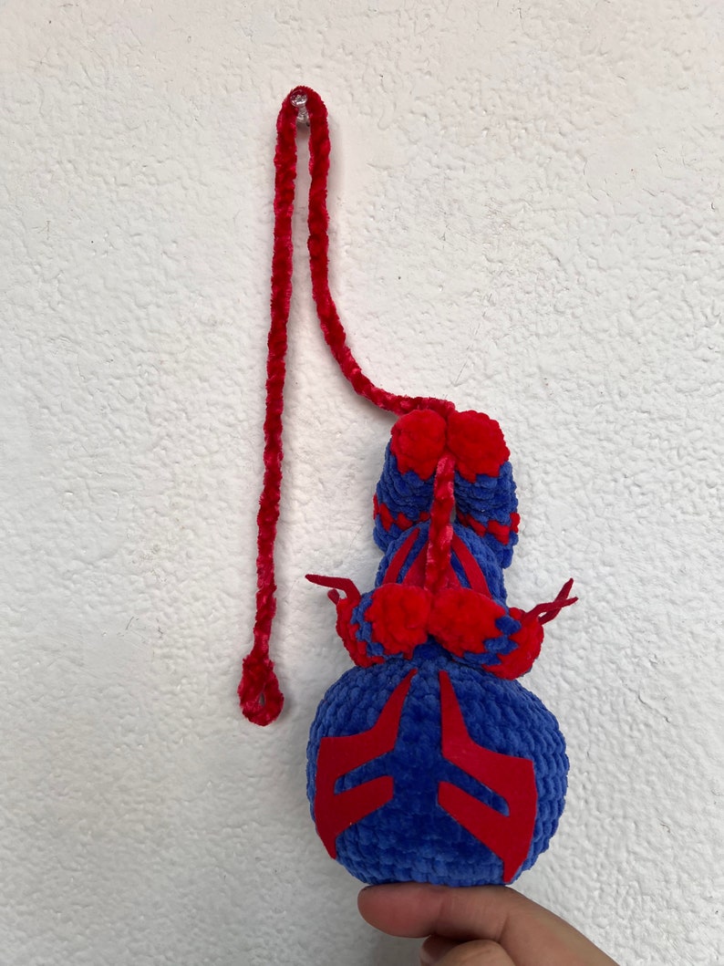 May include: A blue and red crocheted toy with a long red cord. The toy has a round body with red accents and a long, thin tail.