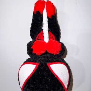 May include: Black and red crocheted plush toy hanging from a white string. The toy has a spider-like design with white eyes.