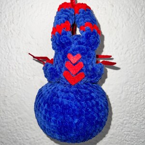 May include: A blue and red crocheted plush toy shaped like a spider hanging from a red string. The spider has three red hearts on its body.