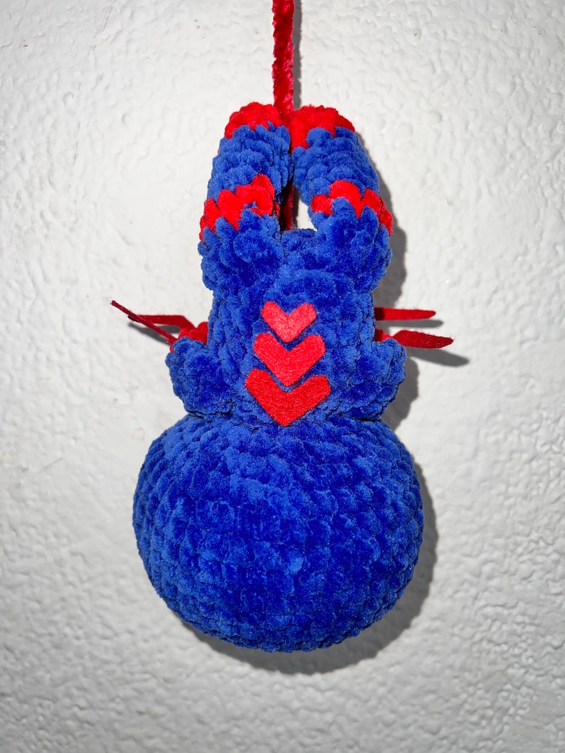 May include: A blue and red crocheted plush toy shaped like a spider hanging from a red string. The spider has three red hearts on its body.