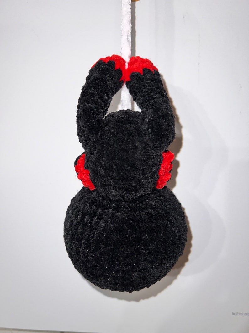 May include: Black crocheted spider hanging from a white string. The spider has red accents on its legs and head.