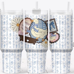 May include: A white tumbler with a handle and a straw, featuring a whimsical design. The design includes a duck wearing a blue bow, daisies, and vintage-style stamps. The background has a blue floral pattern.