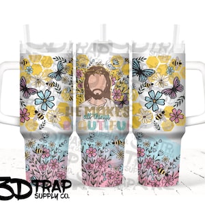 May include: A white tumbler with a handle, straw, and a wraparound design. The design features Jesus with a crown of thorns, butterflies, bees, and flowers. The text "He makes all things beautiful" is also included.