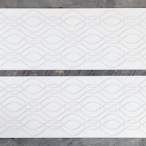 May include: Two white blank tickets with a decorative pattern of overlapping ovals. The tickets are on a wooden surface.