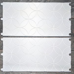 May include: Two white interlocking floor tiles with a repeating pattern of overlapping circles.