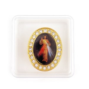 Può includere: Un ciondolo ovale color oro con un bordo di strass trasparenti. Il ciondolo presenta un'immagine colorata di Gesù Cristo con un cuore rosso e bianco. Il ciondolo è esposto in una scatola di plastica trasparente.